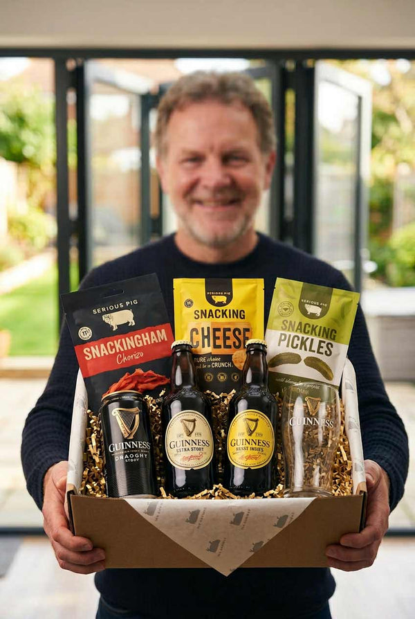 Man holding a gift box with Guinness beer, snacks, and a candle.